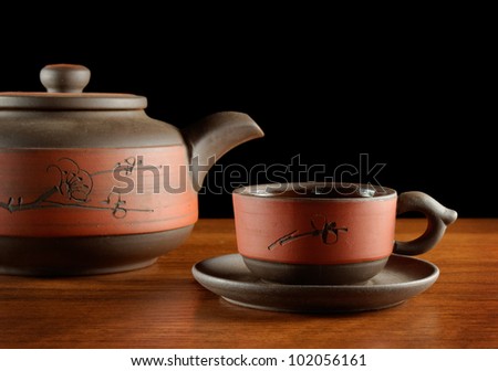 closeup of tea kettle and cup, red and brown color, black background