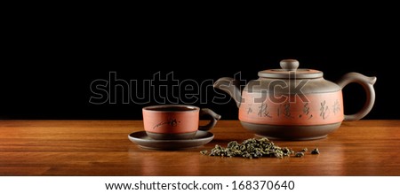 asian style tea set and heap of dry tea on wooden desk, black background