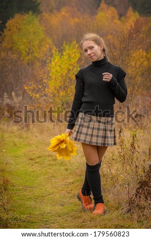 girl in tartain pleated skirt with autumn leaves walks along the forest