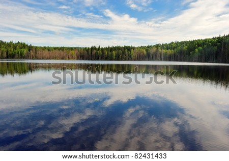 round forest lake, reflecting trees, sky and clouds