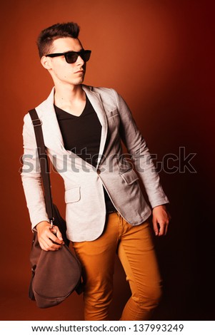 Fashion guy portrait with jacket and sunglasses on orange background studio