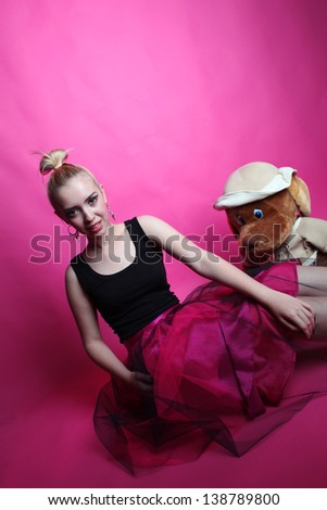 Young lady posing in the studio on a pink background with a teddy bear