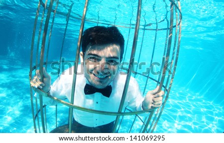 Funny groom underwater in a bird cage