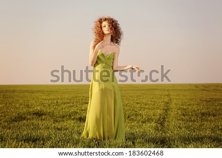 Beautiful styled woman with a long green dress on fields