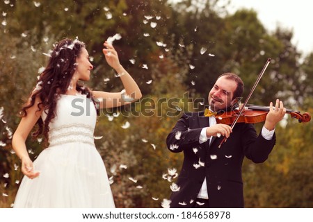 Funny bridal couple, groom playing violin and bride playing with feathers