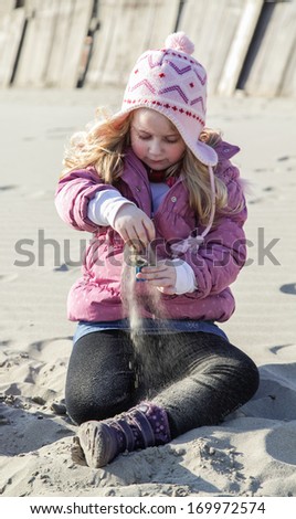 Girl seating and playing on sand during nice winter day