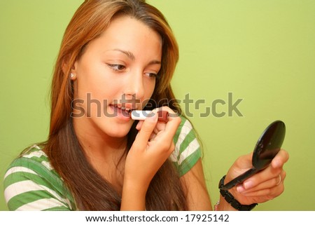 Brown haired teen girl with lipstick and hand mirror doing make-up