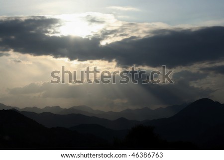 Cloudy sky with sunbeam over mountains looks like light beam from heaven