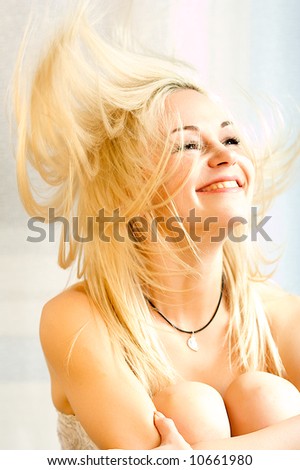 A picture of a young blond woman, tossing her hair as she beams widely, hugging her knees to her chest.