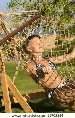 White model lies in the hammock on a background of green branch on the beach.