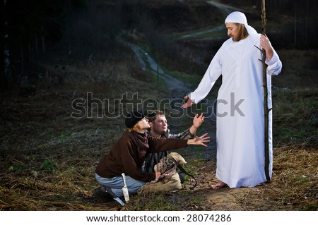 Two people in modern clothing pleading at feet of biblical man holding staff, countryside night scene.