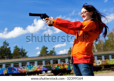 Young woman with long black hair holds a pistol and aims. Railway station.