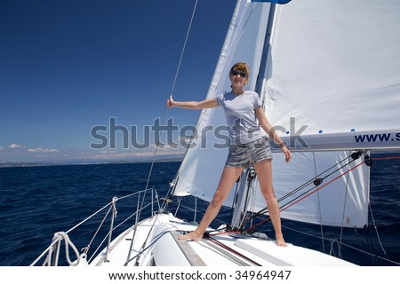 Young woman stands at the bow of yacht. The boat floats on the sea by the wind.