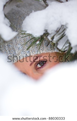 Portrait of a beautiful young woman under a branch of pine tree covered in snow. Face partially hidden by snow.