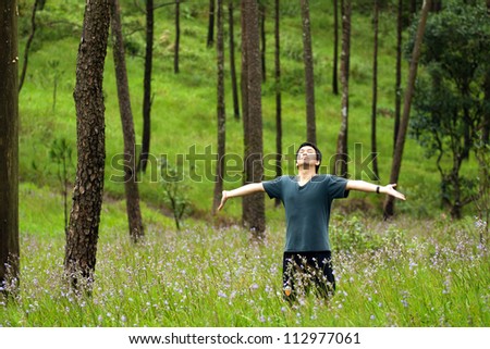 Young man arms raised enjoying the fresh air in green forest.