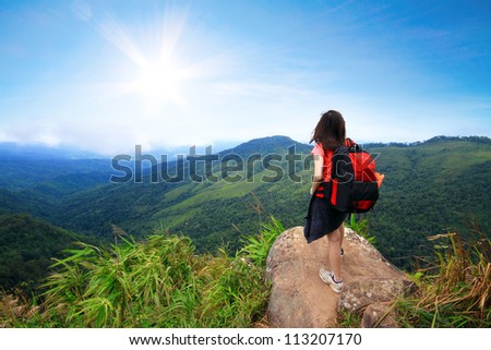 Young woman with backpack stand on a cliff looking at the blue sky