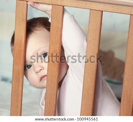 Adorable funny baby boy looking out the wooden bed with big eyes