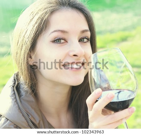 Woman drinking red wine on nature green background. Closeup portrait of young beautiful smiling girl