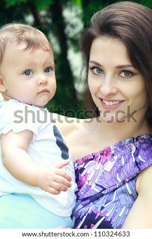 Beautiful young mother holding baby girl on hands and happy smiling on nature summer green background. Closeup natural portrait