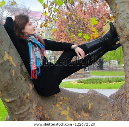 Thinking woman sitting on tree and relaxed looking up with smiling on autumn colorful background