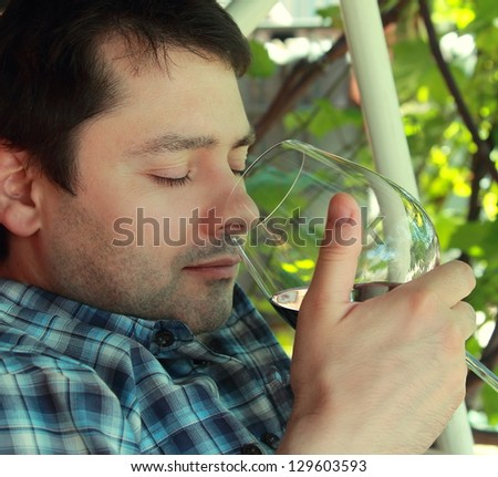 Relaxed man drinking red wine outdoor summer green background with opened eyes. Closeup portrait