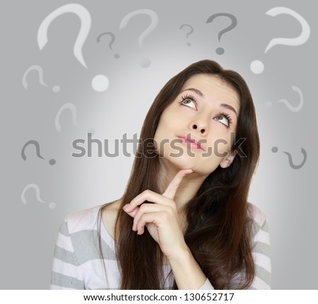 Beautiful girl with questions thinks above her head looking up isolated on grey background Beautiful girl with questions thinks above her head looking up isolated on grey background