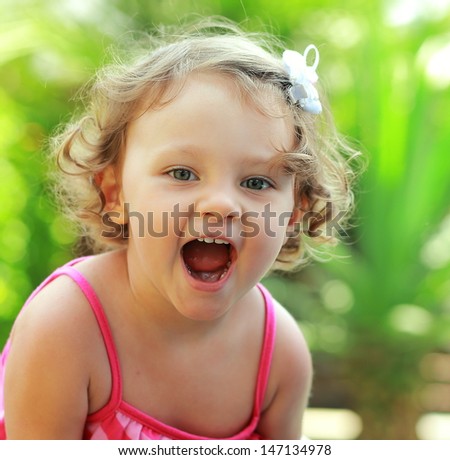 Happy baby girl joy with opened mouth outdoor summer background. Closeup