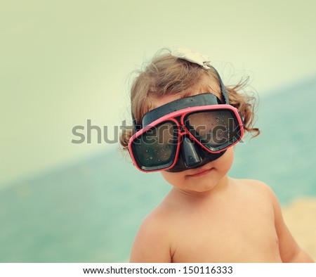 Happy child girl in diving mask smiling on beach background. Vintage closeup portrait
