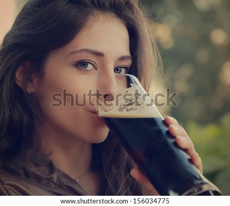 Woman drinking dark fresh beer outdoor and enjoying. Closeup vintage portrait