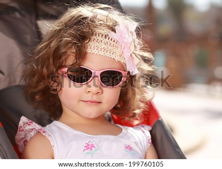 Beautiful small girl with curly hair and pink sunglasses smiling