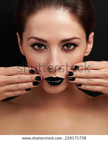 Beautiful bright evening makeup woman, black nails polish and black lipstick looking serious on black background