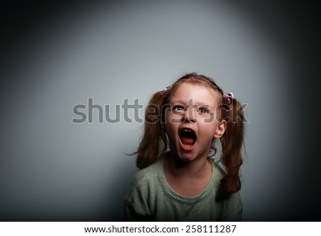 Angry child girl screaming with opened mouth and looking up with evil on dark background