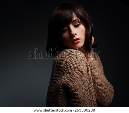 Sexy makeup female model posing in warm wool sweater on dark shadows background