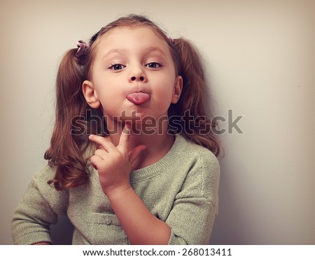 Thinking grimacing girl showing tongue with finger under face and looking funny in camera. Vintage closeup portrait