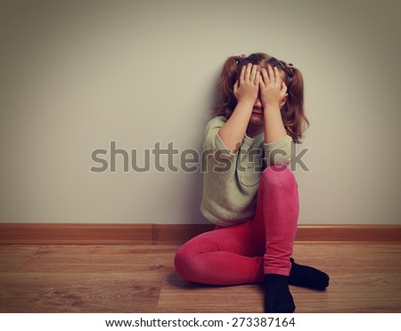 Frightened crying kid girl sitting on the floor with closed face the hands. Vintage closeup portrait