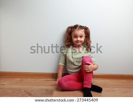 Fun grimacing girl sitting on the floor and smiling on blue wall background