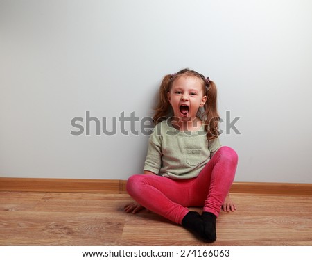 Happy crying kid with open mouth sitting on the floor in fashion clothes