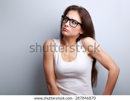 Anger young casual woman in glasses thinking and looking up on blue background with empty copy space