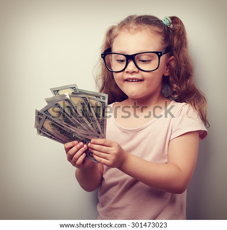 Thinking fun small kid girl in glasses counting money in the hands with grimacing emotion face. Vintage closeup portrait