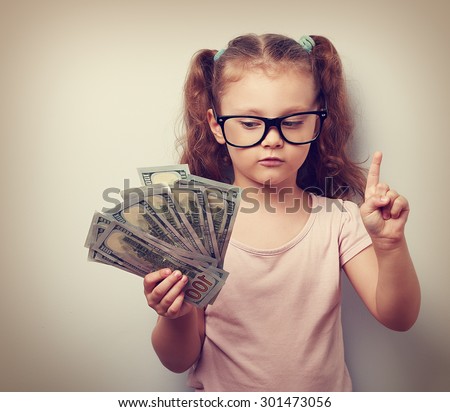 Small kid girl holding dollars and have an plan how earning much money in crisis. Serious child showing finger. Vintage closeup portrait