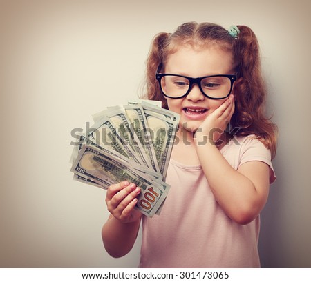 Surprising emotional kid girl holding dollars in hand and thinking how much money she have earned. Vintage closeup portrait