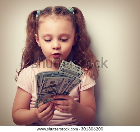 Fun grimacing kid girl looking and counting money in the hands. Vintage closeup portrait