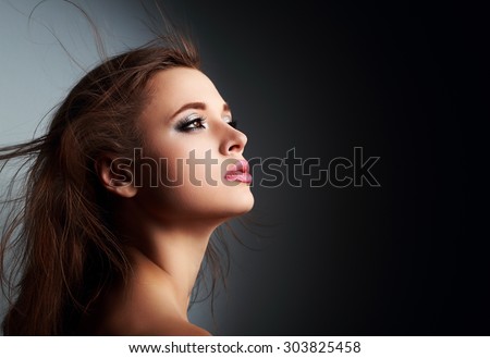 Beautiful makeup woman profile with long hair looking up with hope on dark shadows background