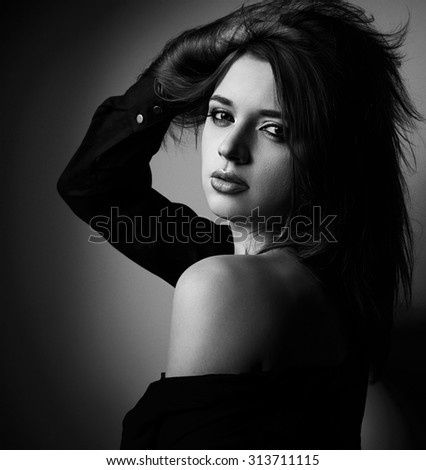 Sexual beautiful woman in black shirt posing with nude shoulder on dark background. Black and white closeup portrait