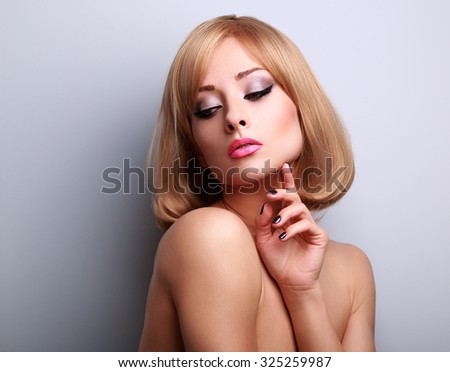 Beautiful makeup woman with perfect clean skin looking down and touching fingers the face on blue background with empty copy space