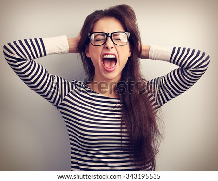 Angry young business woman in glasses strong screaming with wild open mouth and holding head the hands. Toned closeup portrait