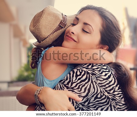Happy mother hugging her daughter with love and natural emotion with closed eyes. Closeup toned portrait of family love