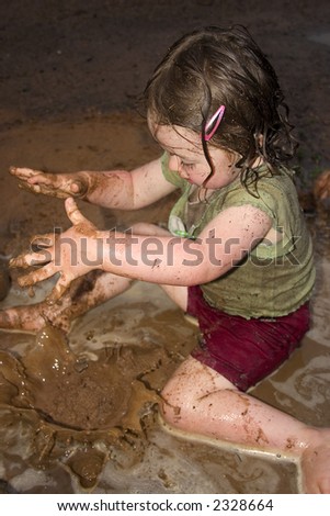 a little girl dropping mud into a puddle