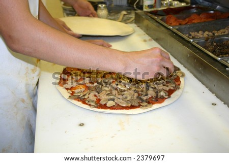 a guy putting toppings on a pizza
