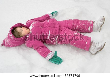 a serious little girl making a snow angel